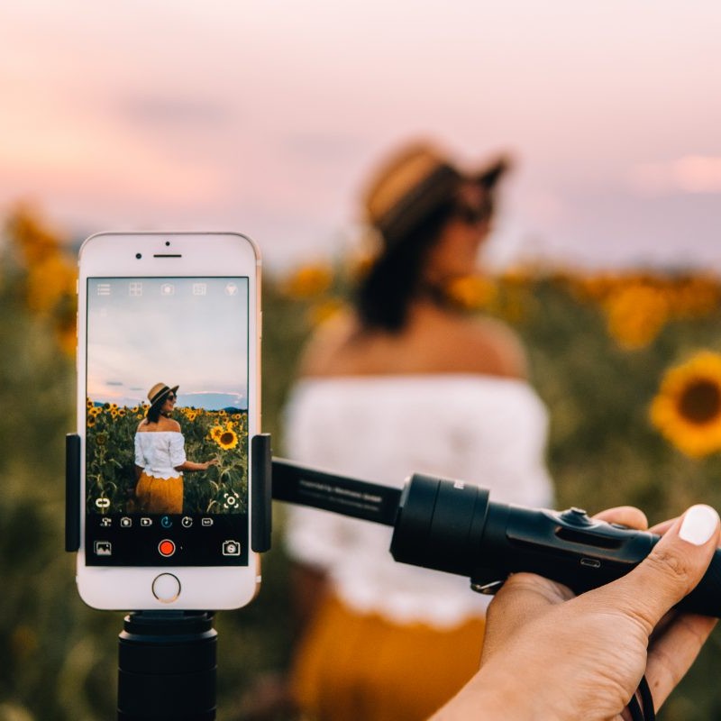 Jana steht in einem Sonnenblumenfeld mit ihrem Smartphone bei der Reisefotografie