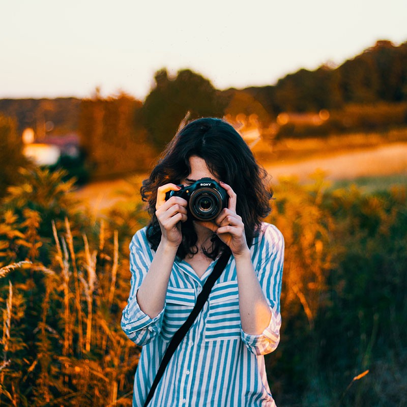 Eine Frau steht im Sommer auf einem Feld und fotografiert. Die schönste Beschäftigung fürs lange Wochenende.