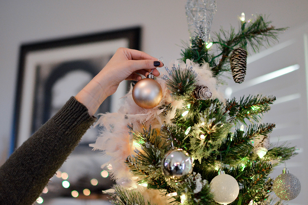Weihnachtsbaum wird mit Federn, silbernen und weißen Kugeln geschmückt