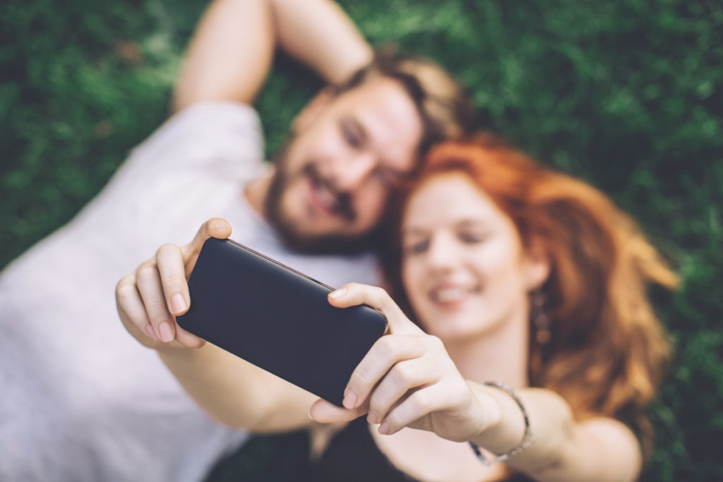 Paar liegt auf grüner Wiese und macht Selfies