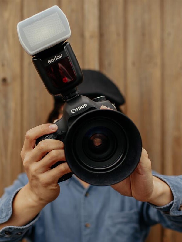 Mann hält eine Spiegelreflexkamera mit Aufsteckblitz vor sein Gesicht