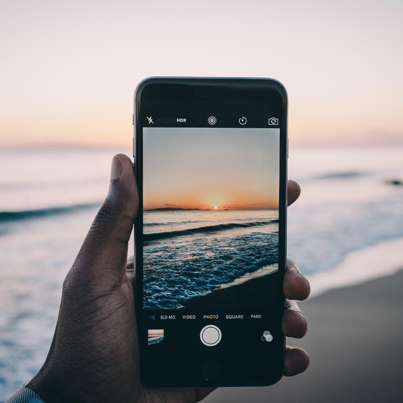 Mann fotografiert mit seinem Smartphone den Sonnenuntergang am Strand