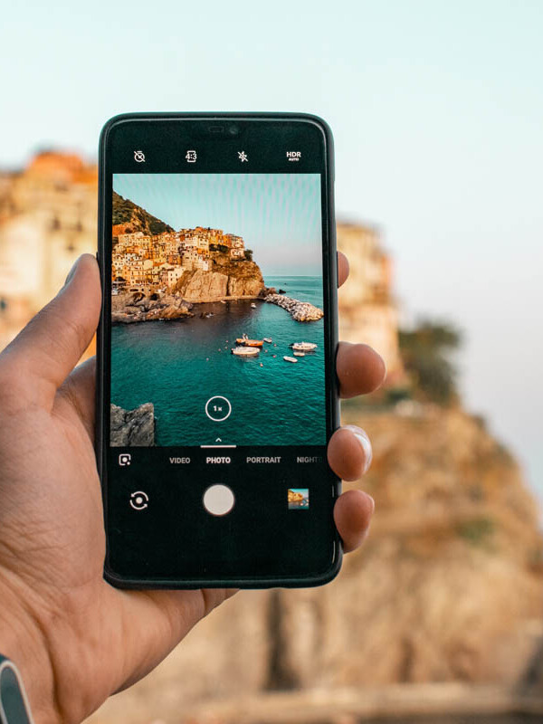 Mann fotografiert eine Küstenstand in Italien mit dem Smartphone