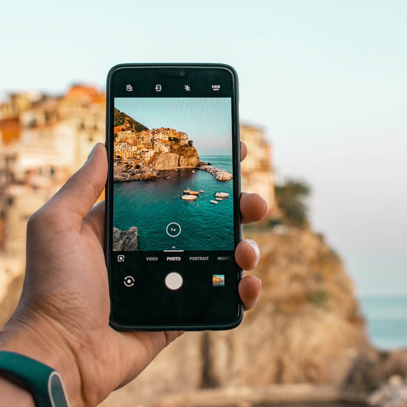 Mann fotografiert eine Küstenstand in Italien mit dem Smartphone